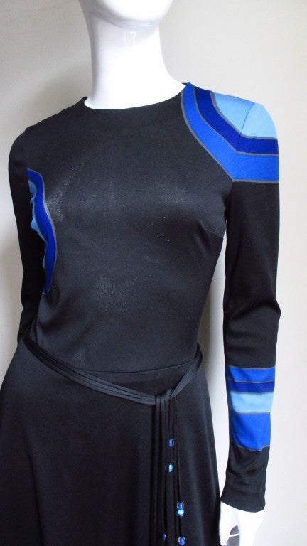 A full length long sleeved synthetic jersey dress by Louis Feraud with large circles and stripes in various shades of blue on a black background.  A crew neck fitted bodice with a long skirt flaring at the hemline. Beautiful brightly colored shapes