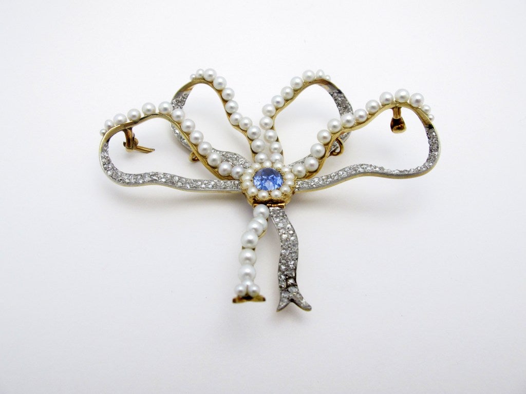 Exquisite platinum topped gold bow brooch set with a central faceted oval blue sapphire of approximate total weight 3 carats,  70 natural pearls averaging 3.5mm, and 250 rose-cut diamonds of approximate total weight 2 carats.