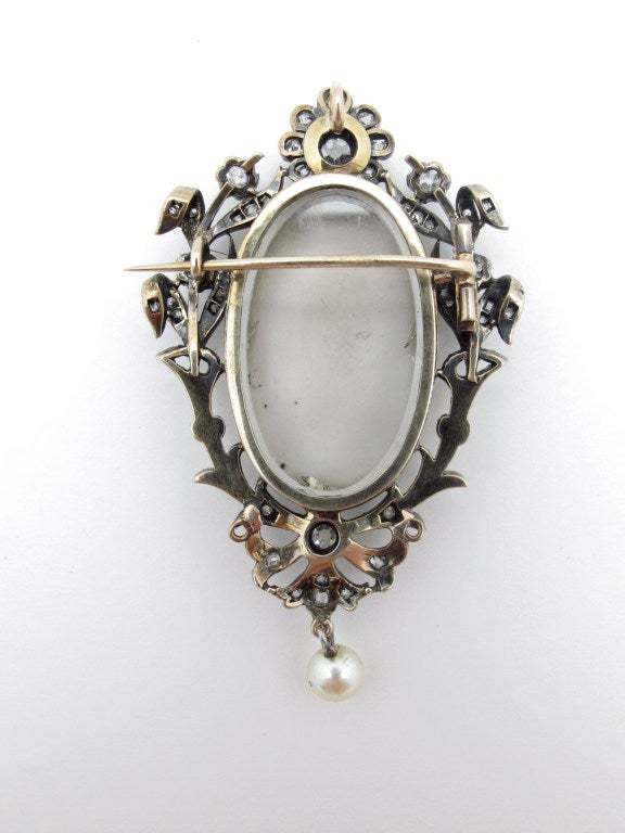 This silver topped gold pendant/brooch depicts a female figure in  a diaphanous gown accompanied by a putto beautifully painted on copper. It contains 77 old mine cut diamonds of  approximate total weight 2 carats, color: I-J clarity: SI. The