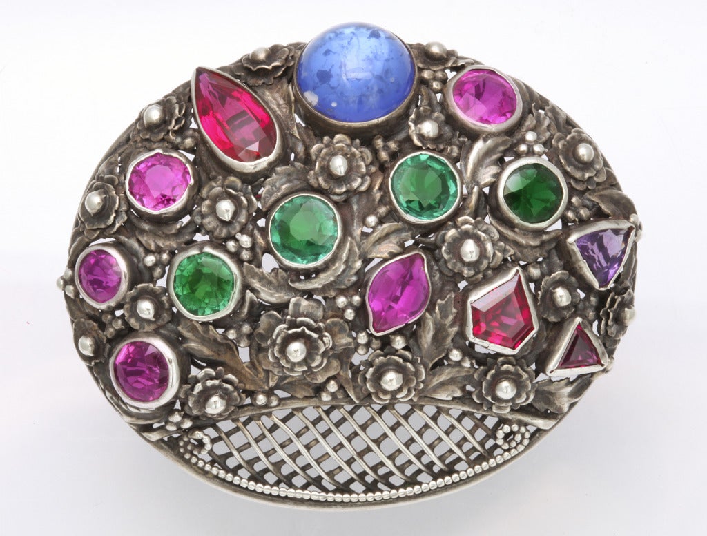 A large and colorful Hobe brooch as a stylized flower basket of sterling silver set with sparkling colored crystal jewels. Hobe and sterling silver marks. 2 1/4 inches x 2 3/4 inches.
From the Hollywood estate of a 50 year collection. Please watch