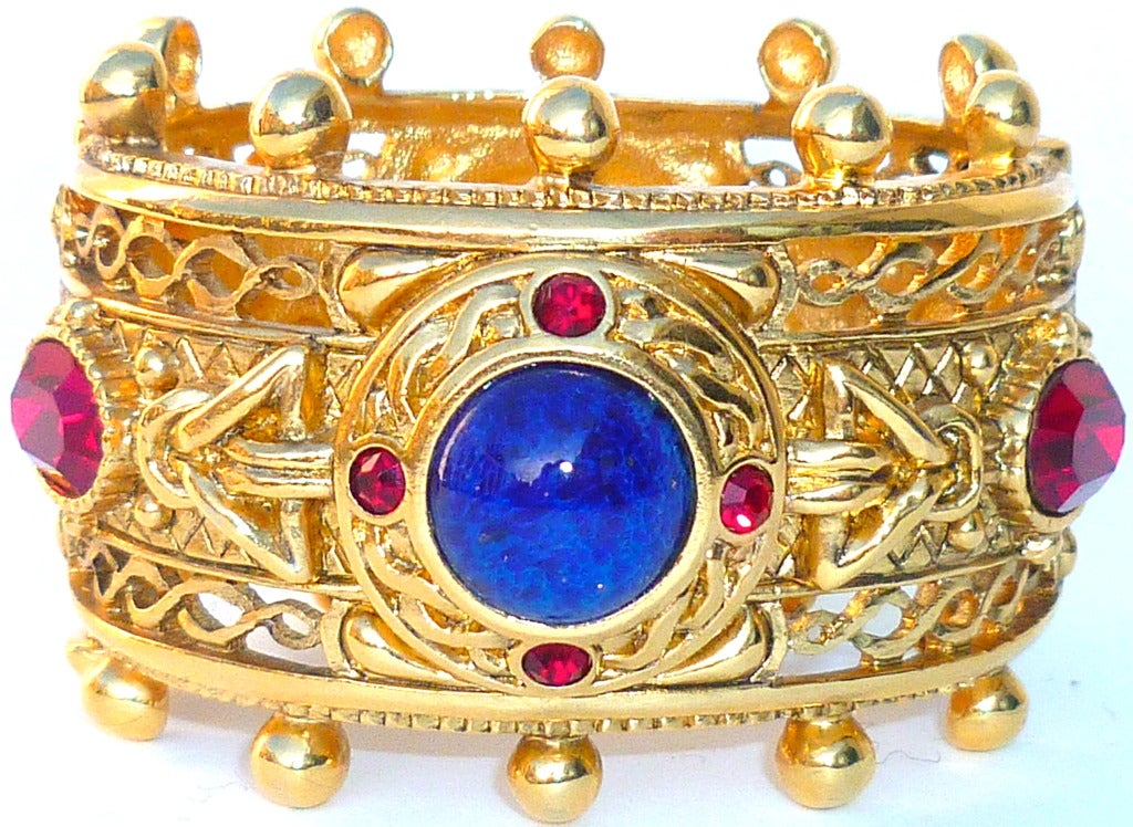 Beautiful  Byzantine style Christian Dior cuff bracelet made by Robert Goossens. Substantial and detailed gilded openwork metal frame encasing large Swarovsky crystals of ruby and sapphire color, and a deep blue glass cabochon imitating lapis.
