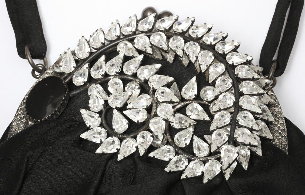 A spectacular 1930s black silk evening bag, the frame features a black stone anchoring three curled and overlapping metal plumes set with large tear drop crystals, the interior of cream silk, with label reading: 