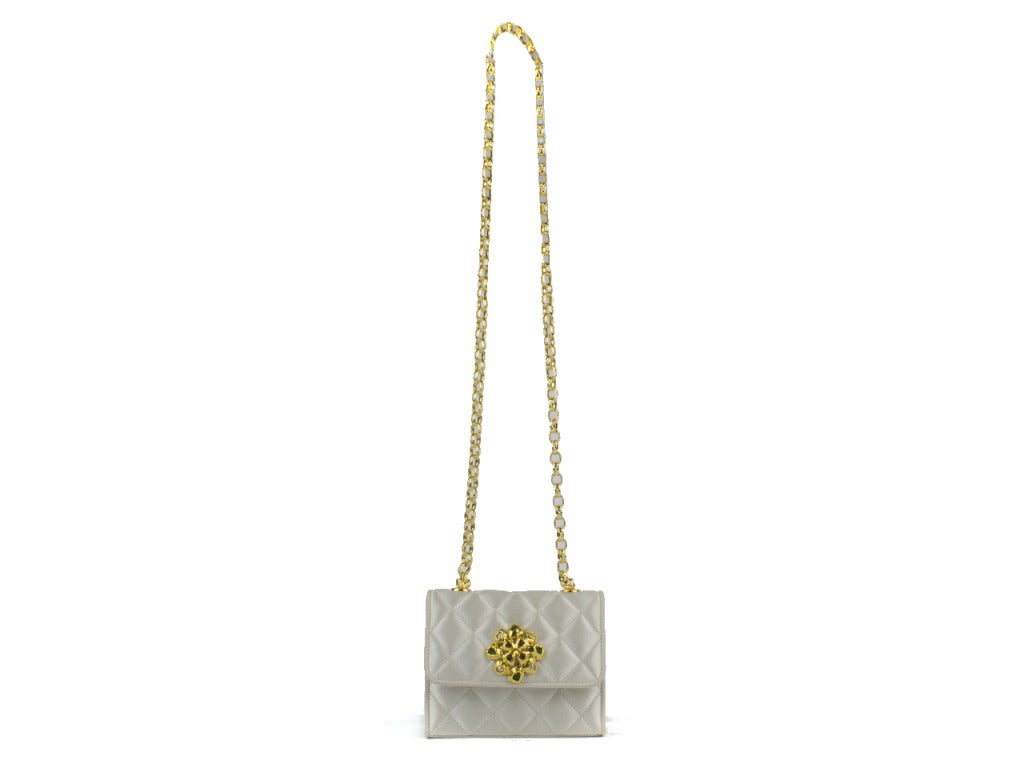Baby, it's cold outside. Why not make your style warmer with this white satin quilted Chanel gripox bag with a stunning red, green and white jeweled broach on the flap and shiny gold chain!