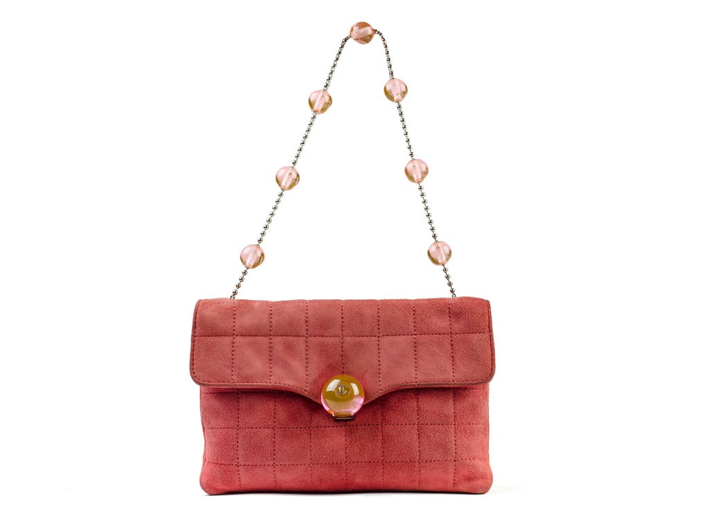 The Chanel suede red bag boasts a utilitarian folded body and unique bohemian charm. Quilted medium red suede is jazzed up with opaque red marble-like glass beads on a silver chain strap. A single bead on the end of the flap shows silver