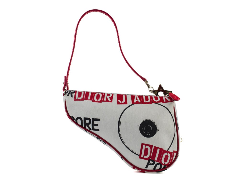 Own a hardcore piece of fashion history! The limited edition Christian Dior Hardcore small saddle bag features white canvas body in unique saddle shape with black and red print, red leather piping and strap and silver star and body piercing hoop