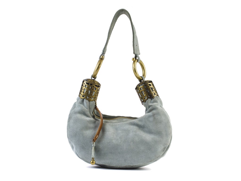 Eclectic yet sweet, the Chloe bracelet bag is the ideal companion for a maxi skirt and fun embellished sandals on faraway vacations or adventures closer to home. The light blue suede handbag conforms into a U shape with genie-in-a-bottle-like bronze
