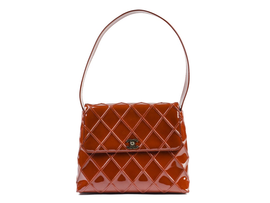 Dare to be different with this beautiful Chanel shoulder bag. It has a unique burnt orange patent leather exterior with quilted stitching, and a classic flap with turn lock. Has a thick solid strap that is 10
