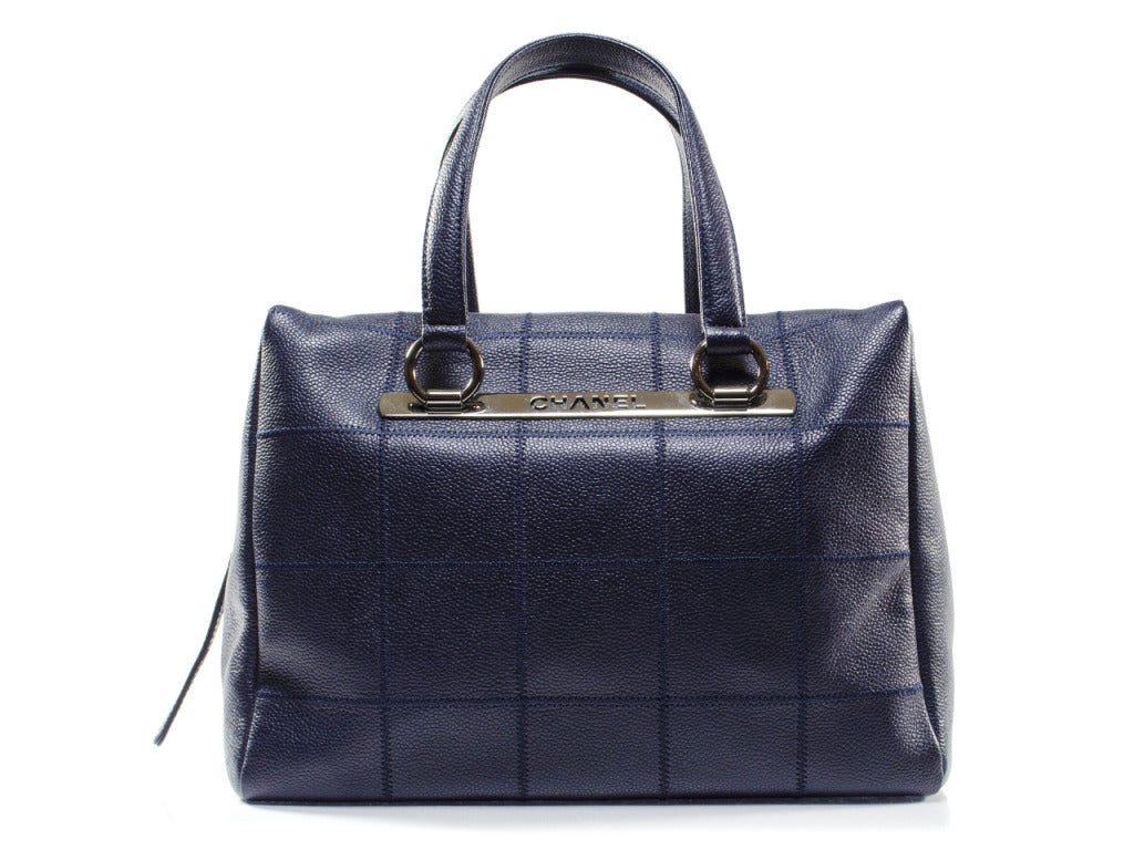 Board your next flight with the finest carry-on balanced on your forearm, the Chanel Cruise caviar leather satchel. Dark navy caviar leather features large square quilting on front and back panels with simple pebbled leather on sides. A dark silver