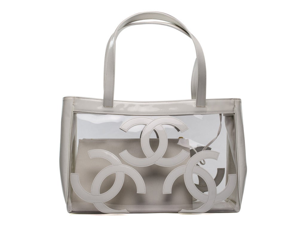 Head to the beach in this fun clear tote! A white patent leather exterior trims the clear vinyl panels while the front and back are adorned with matching patent leather CC logo appliques. Four brass feet protect the bottom of the bag. Also includes