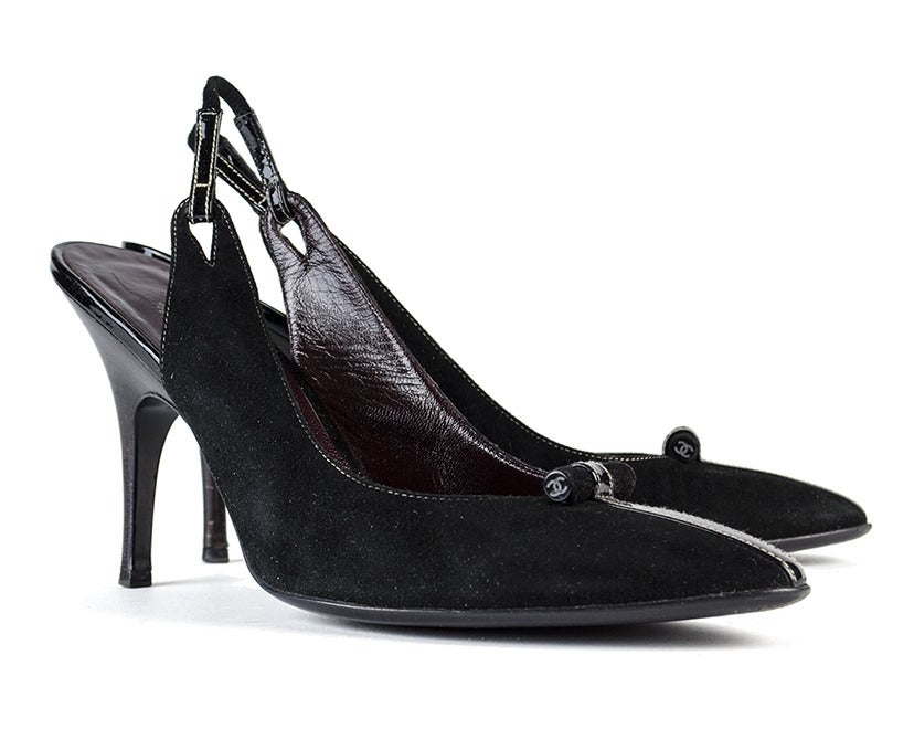Command the board room in understated elegance with the Chanel black suede slingback heels. Circular piece at front is imprinted with white interlocking 'CC' symbol on either side and affixed with a patent leather strip from vamp to toe, creating a