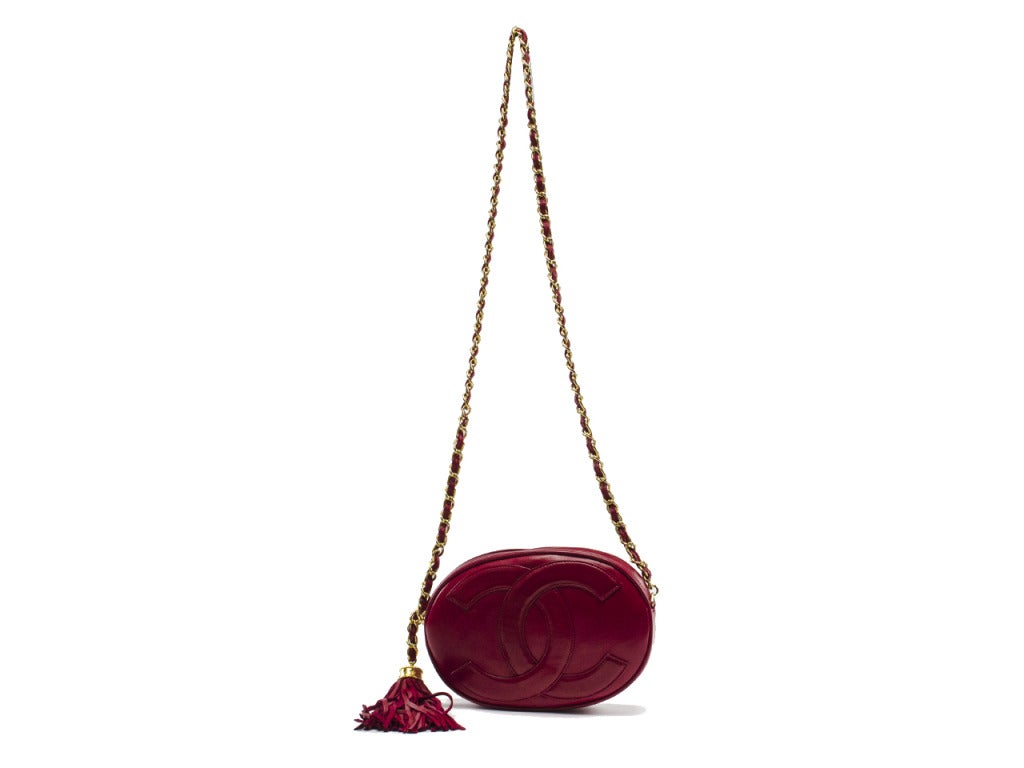 Vintage Chanel at its best. This unique cherry red leather camera bag calls attention with classy curves and sassy adornments. Interlocking CC symbol embellishment covers entire face of oval shoulder bag while yellow gold chain link strap and red