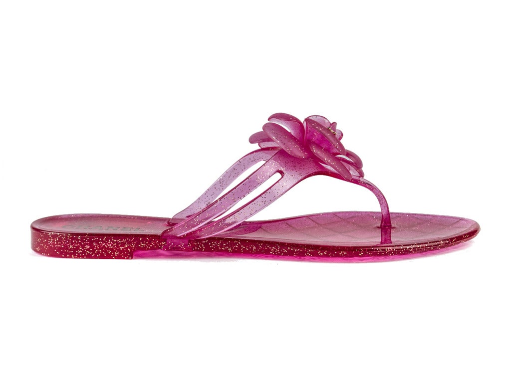 Sparkle through the summer months in neon pink Chanel jelly sandals. Flower details with gold interlocking ‘CC’ charms on petals and a gold stud at center adorn the top of the thong, adding just the right amount of feminine flair. Condition: Item is