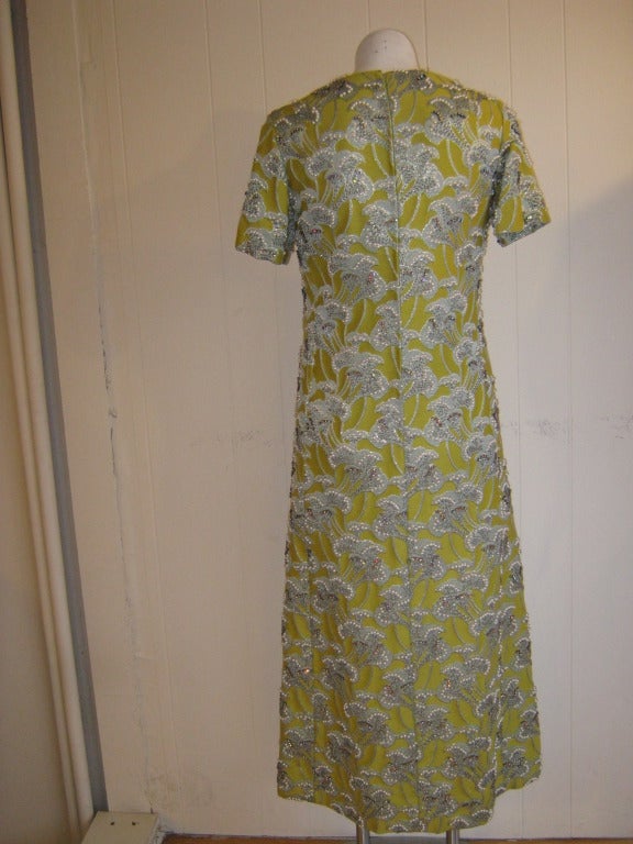 This dramatic lined rayon dress beaded with pearls, stones on a raised fab shaped leaf/flower pattern with interwoven gold thread, was created by Diane Imports in the 1960s.

The dress has a fairly high neck line, short sleeves, and is slightly