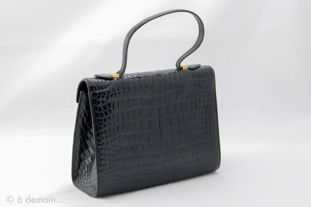 Rectangular Pierre Cardin Boutique Paris handbag, with his short shoulder strap, it is in black crocodile porosus, and gold garniture. Clasp invisible to the front, a large central pocket, and a little one to the inner side. From the 1980s.
Good