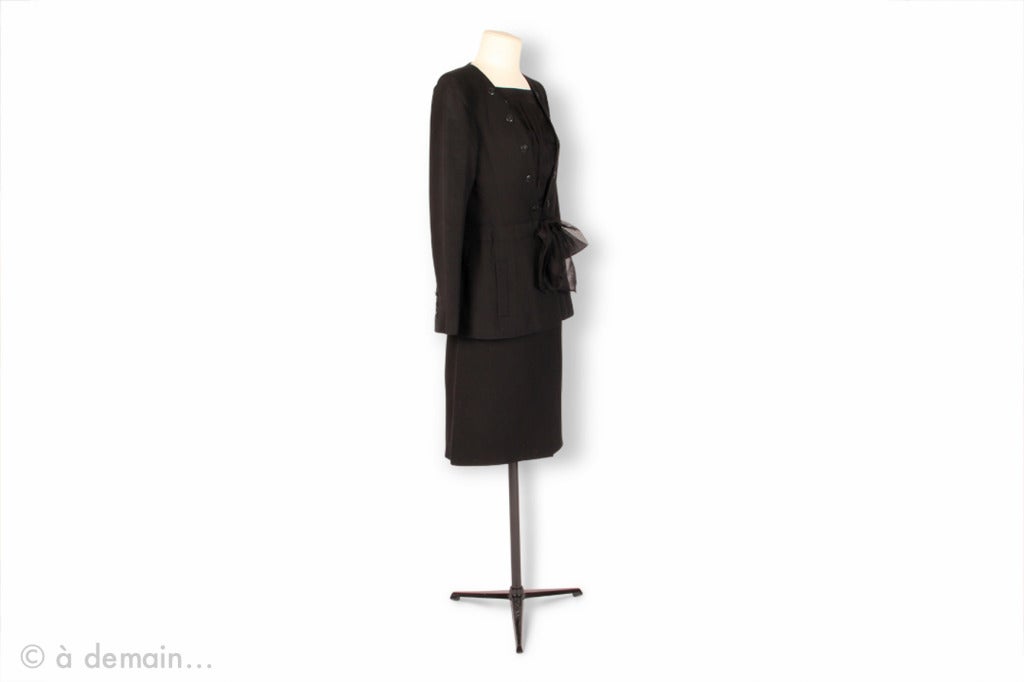 Chanel black suit of black embossed cotton, including a taken in at the waist jacket with a silk blouse at the neckline, a black silk belt, and a matching straight skirt. Model from 2000. 

Condition: Excellent 
FR size: 40