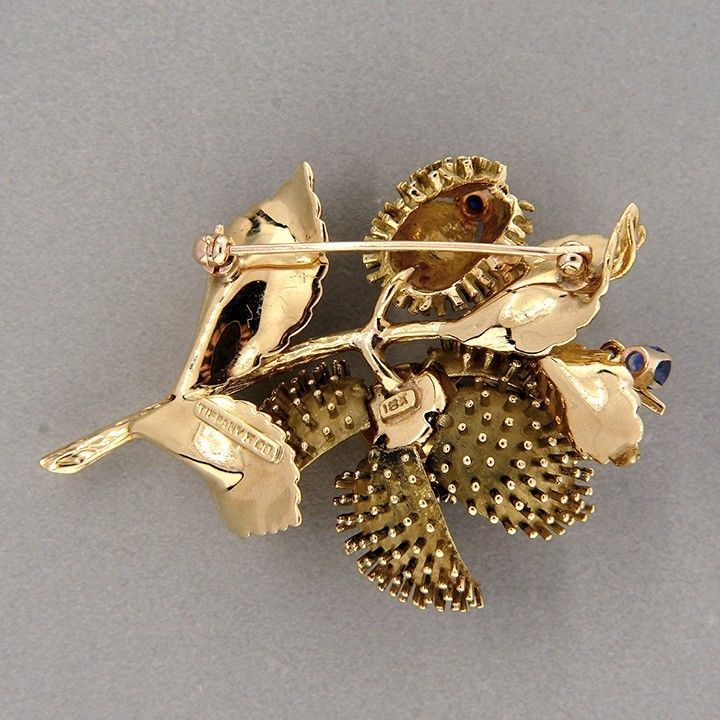 1960's Tiffany + Co solid 18k yellow gold flower pin with one section that opens and closes to reveal a bright blue Sapphire diamond flower. 3 dimensional and highly detailed. 

1 round full cut diamond, approx. total weight .12ct, F, VS1   