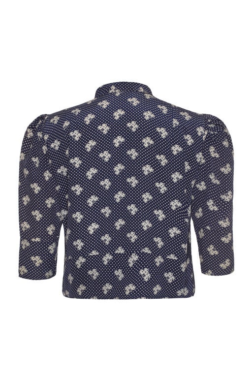 Beautiful silk blouse in navy featuring a cream floral and polka dot design.  
This versatile piece has  ¾ sleeves that gather at the shoulder, and it fastens at the front with hook and eyes. Perfect for an elegant ensemble, and in excellent
