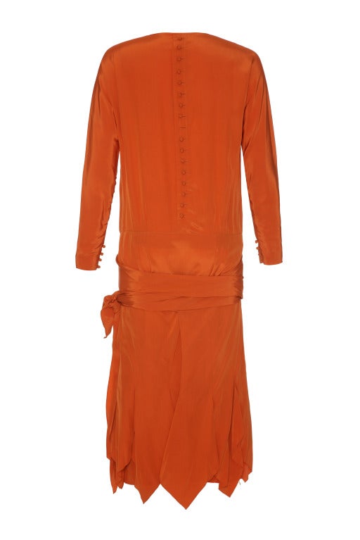 A beautiful long sleeved silk flapper dress with a wrap-around skirt layer tying at the dropped waist.  
The dress is beautifully pin-hemmed and features a false fastening of matching covered buttons down the back. 
The vibrant rust colour of the