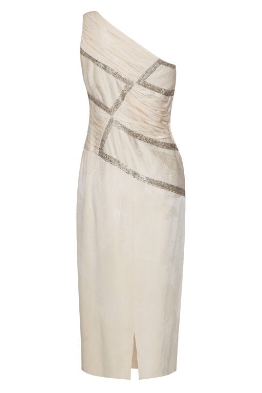 The bodice of this late 1950’s white silk dress by Minx Modes is made up of rouched and embellished panels with geometric detailing in silver bugle beads. Look closely and you’ll see the silk has a subtle textured leaf pattern.  With the asymmetric