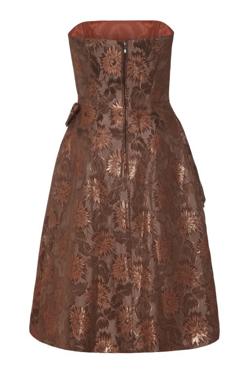 A really gorgeous and easy to wear 1950’s cocktail dress by Jonelle. The outer brocade is made up of various tones of bronze, some with metallic thread woven into them. The design features asymmetrical layers to the front with two cute bows in the
