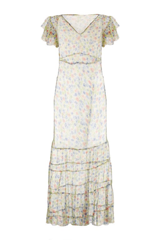 This original late 1920's or early 1930s blue, green and orange floral print dress has an elegant deep tiered flounce at the bottom and double tiered ruffle capped sleeves. As with many silk chiffon floral tea gowns, the dress is sheer and therefore
