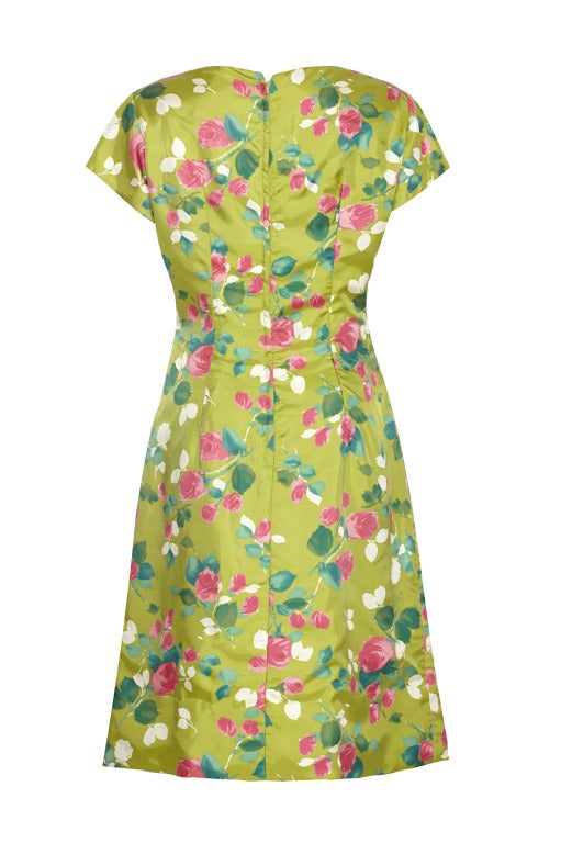 Colourful faux silk lime green 1960’s dress with bright pink roses.  The dress is fitted with a deep hem line, short capped sleeves and fastens at the side with a metal zipper.  There is a bow detail on the bust line and four ornamental buttons on