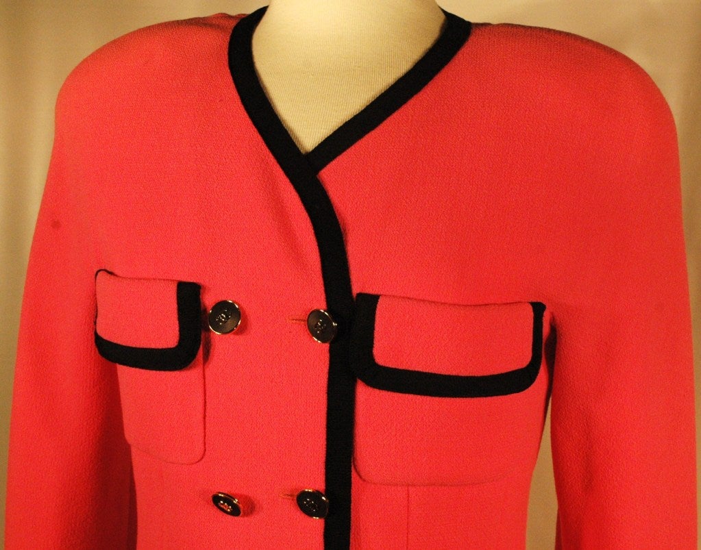 Iconic  Hot pink Chanel wool crepe jacket and skirt set from the 1980s. The jacket is double breasted, trimmed in black with a black bow at the hem, has two front pockets, six gold and black Chanel logo buttons, and is lined in pink silk printed