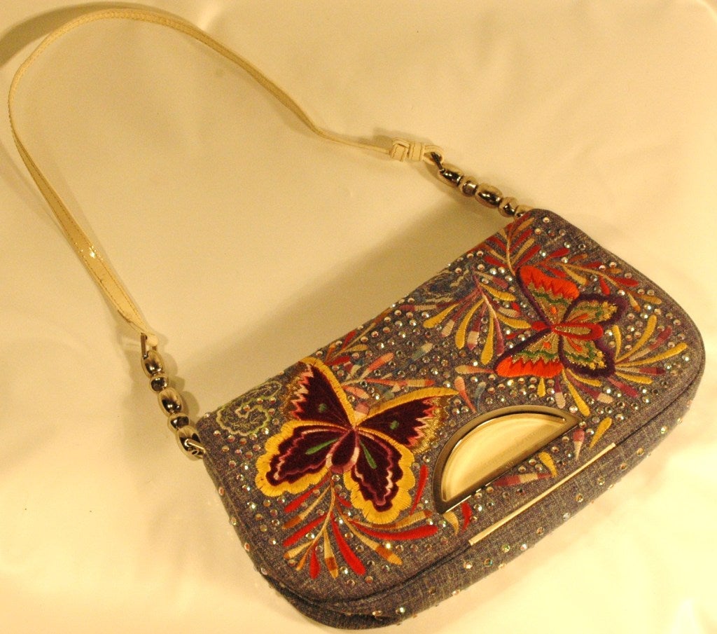 This is a Christian Dior denim flap handbag with embroidered multi color butterflies and aurora borealis crystal with a white patent leather handle and silver hardware.
Made in Italy
Measures 11