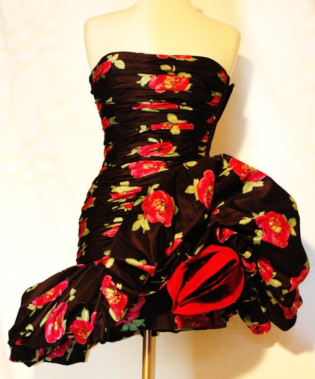 This is an incredibly sexy Emanuel Ungaro strapless rosebud dress. The strapless dress in a hot pink floral print on black has a boned bodice with a side zipper. There is a fabric rose on the left of the huge fabric gathered ruffle that drapes to