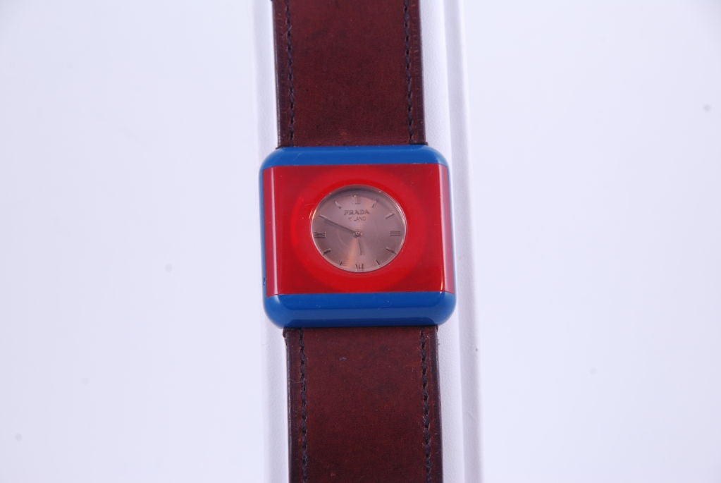 Prada lucite watch in a reddish orange and blue lucite case. The wide band is brown leather. The watch is from 2005. Movement is quartz and Swiss. In good working order.