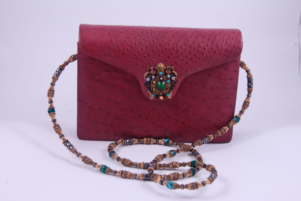 Vintage raspberry colored ostrich evening bag with elegant jeweled clasp and shoulder chain. The piece over the clasp is stylized to resemble Austro-Hungarian jewelry. 

The shoulder chain has hematite crystals that resemble marcasite and green