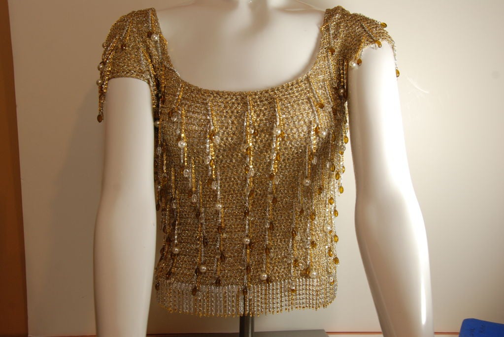 Loris Azzaro gold crochet knit in metallic gold thread. The bottom of the sweater has a fringe made gold gold and silver chain. The same chain is used over the sweater and has either a bronze bead or a pearl attached. <br />
<br />
This does not