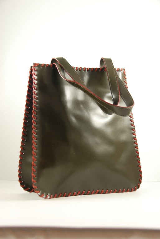 Kenzo olive green over stitched leather bag/tote. Bag is polished leather and the red over stiching is leather was well. The lining is red fabric. There is on open compartment and a zipper compartment inside. The clasp is a magnetic snap and works