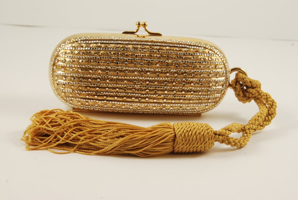 Judith Leiber minaudiere with rhinestones and gold repousse work. The tassel can be used as strap to hold the purse over your arm. All stones are present and the bag sparkles. Clasp works well and bag closes securely.