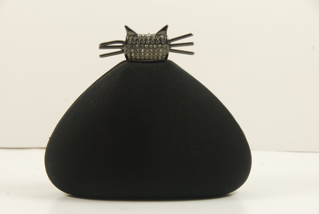 Amusing black satin evening bag in the shape of a cat! The body of the bag is black sating. The clasp which is the outline of the kittys head is blackened metal encrusted in rhinestones, the tail of the kitty curls around the front of the bag.