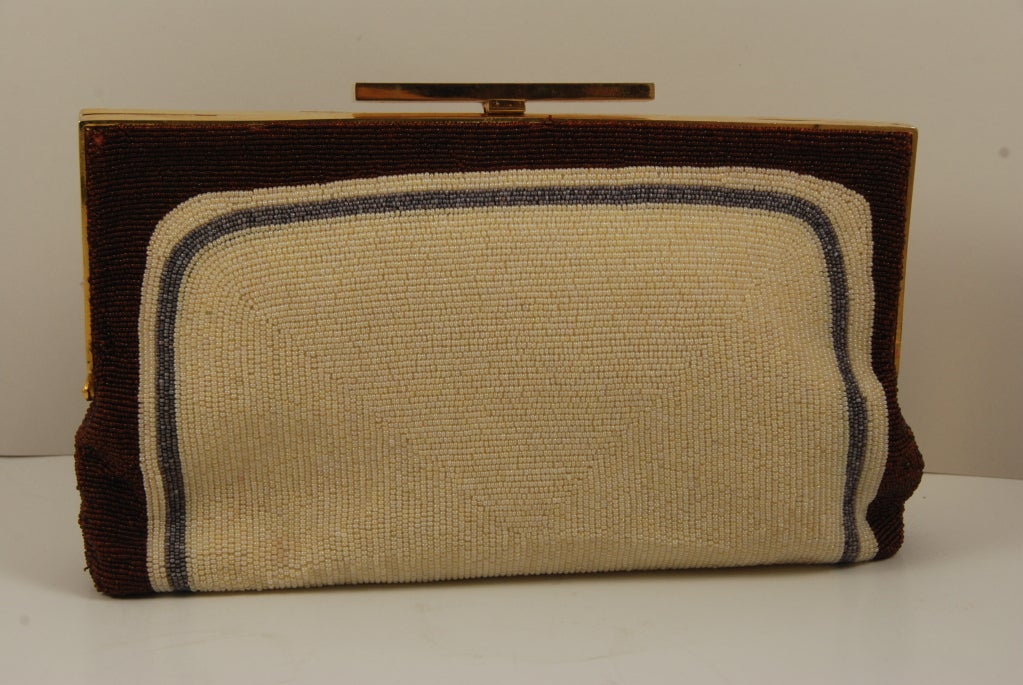 An early design by the French designer Pierre Cardin. This piece is probably from the early 1960's. Beads are coppery brown, grey and off white. The swirl design is on the front. The frame is in gold. There is a chain that can be folded into the bag