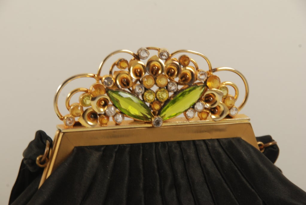 Fantastic black satin evening bag by Josef from the 1950's with jeweled frame. The frame has green, clear and golden rhinestones.  There are also gold metal lilies on the frame.

The body of the bag is black satin and the handle is black satin as