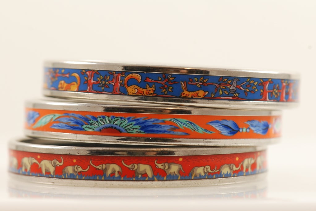 Three Hermes printed enamel bracelets with complementary colors that look well when worn together. The metal banding on all three are in the silver and palladium plating. 

The bracelets are the 65 size.