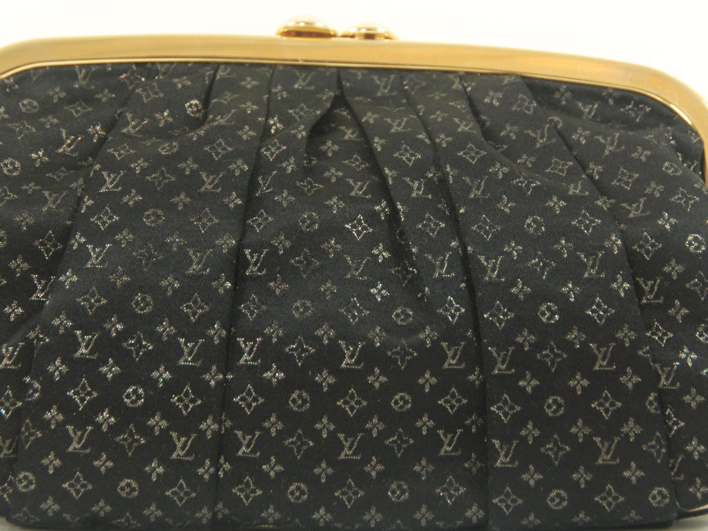 Louis Vuitton black satin evening bag with the LV monogram in a subtle gold undertone. The bag is lined in gold lambskin and there is gold piping along the outer seam of the bag. There is a chain strap that folds inside when not in use with a gold