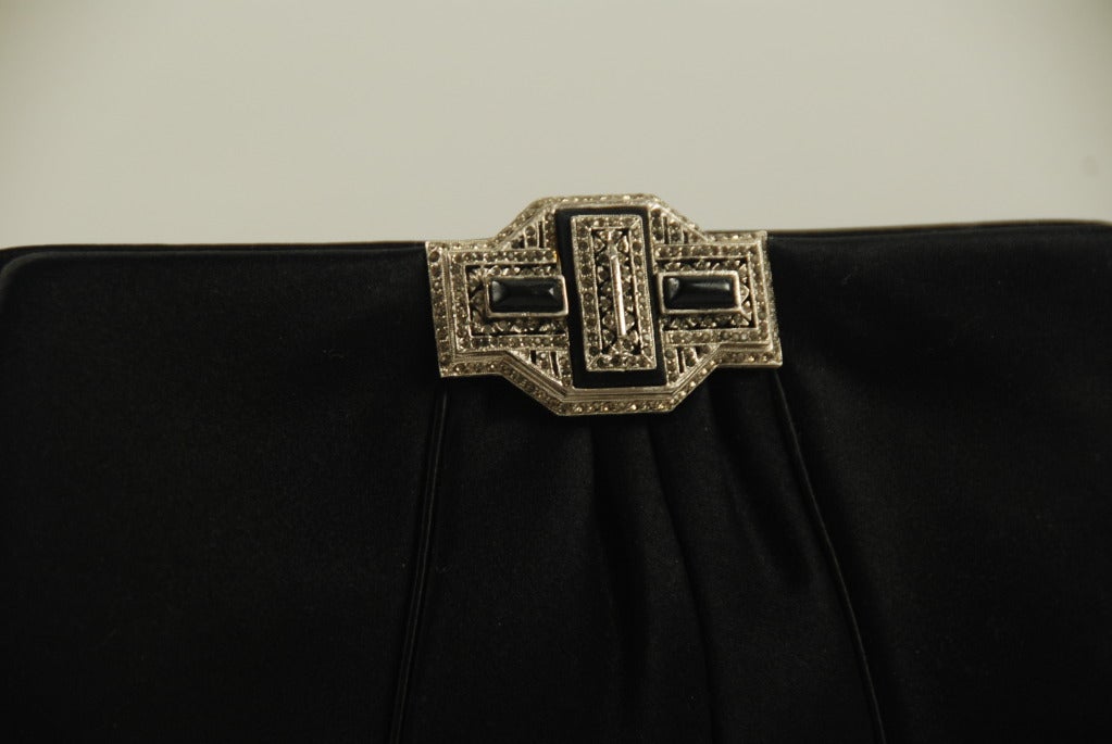 Black satin Judith Leiber evening bag from the 1980's. The clasp of this bag has black onyx stones and black diamond rhinestones that mimic the look of marcasites. This style of clasp was used in the 1910-20's period. This bag has a shoulder strap