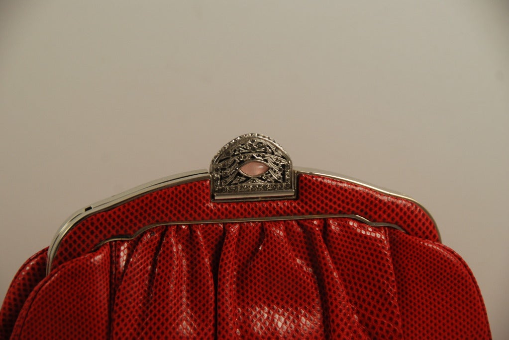 Vibrant red karung (lizard) handbag by Judith Leiber from the 1980's. This bag has an antique style clasp with rose quartz and rhinestones that mimic marcasites that were used in the 1920's. Clasp works well and bag closes securely.

The metal on 