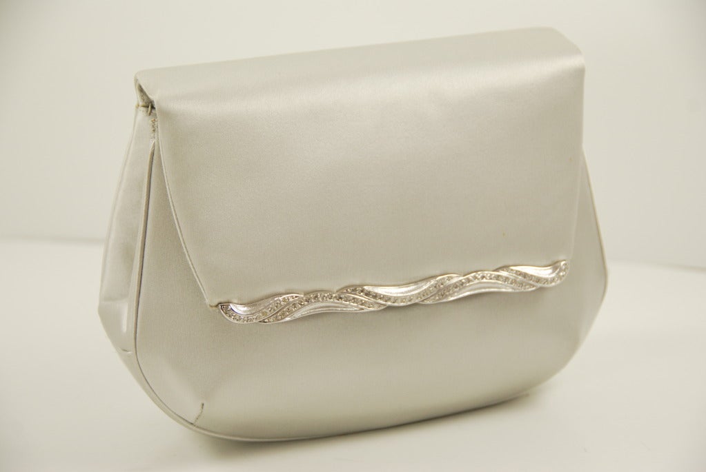 Simple, elegant satin Judith Leiber evening bag with silk rope shoulder strap. Front of the bag has a metal bar studded with crystals in a wave pattern. Platinum silver color is a great neutral color, goes with everything.
