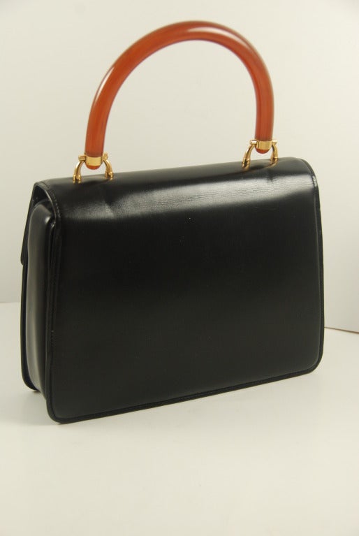 Elegant Gucci black smooth leather handbag with brown Bakelite handle and clasp. Bag is perfect for day or evening and is a classic Gucci style. Interior is black and has one zipper section and three slip compartments. The slip compartments were