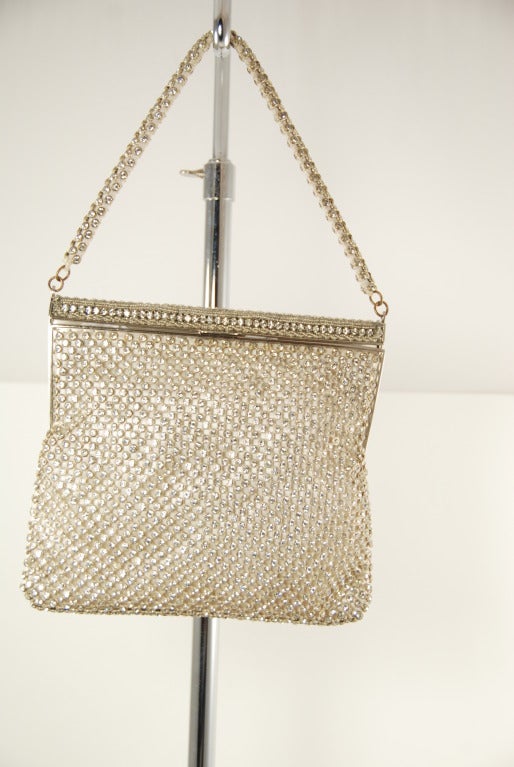 Clear rhinestone mesh over cream color stain evening bag. Each rhinestone is wrapped in a metal setting and woven into a mesh that covers the entire bag. There are no prongs so it wont snag your clothes. Hand strap is covered in the same