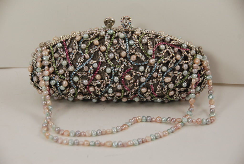 Pearl studded minaudiere by Edidi. There are a platinum lurex lining and background to the pearl and rhinestone design. The colors of the rhinestones are light blue, pink, green and aurora borealis. The metal frame is done in open work and the lurex