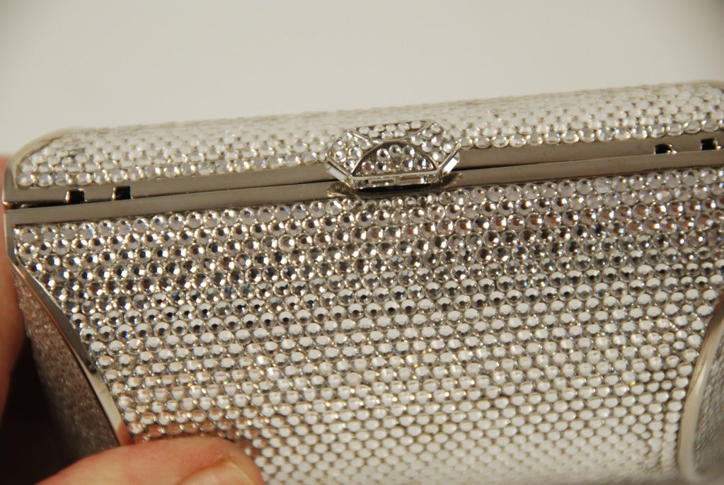 Judith Leiber full bead minaudiere. The rhinestones are all clear and cover the entire bag. The metal is silver tone and there is s strap that folds into the bag when not in use. The strap has a 5