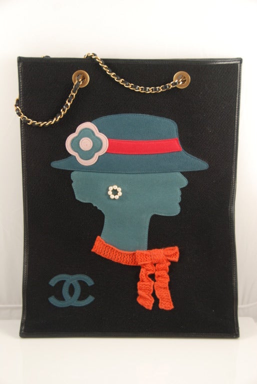 Black Chanel tote bag with the profile of Coco Chanel on the front.wearing the style of hat she was frequently photographed in.. The colors of the bag make this a fun accessory to wear, The black background material appears to be of the fabric used
