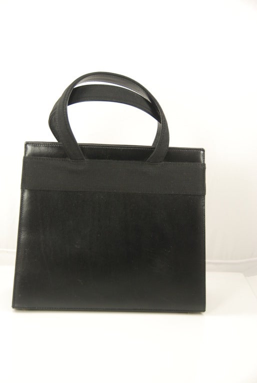 Classic black leather Ferragamo handbag in great condition. In fact, it seems that this bag has never been used, even the shoulder strap is in the original wrapping. A wide black grosgrain ribbon, in a flat bow runs across the front and back of the