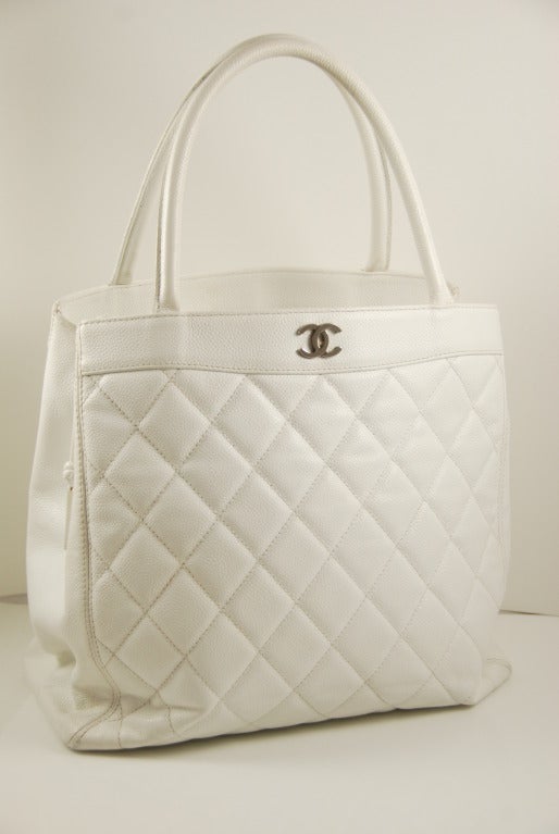 Chanel handbag in white cavier leather in the quilted pattern. This is a larger bag with two open sections and a center section that closes by a zipper along the top of the bag. The handles have a 5.75