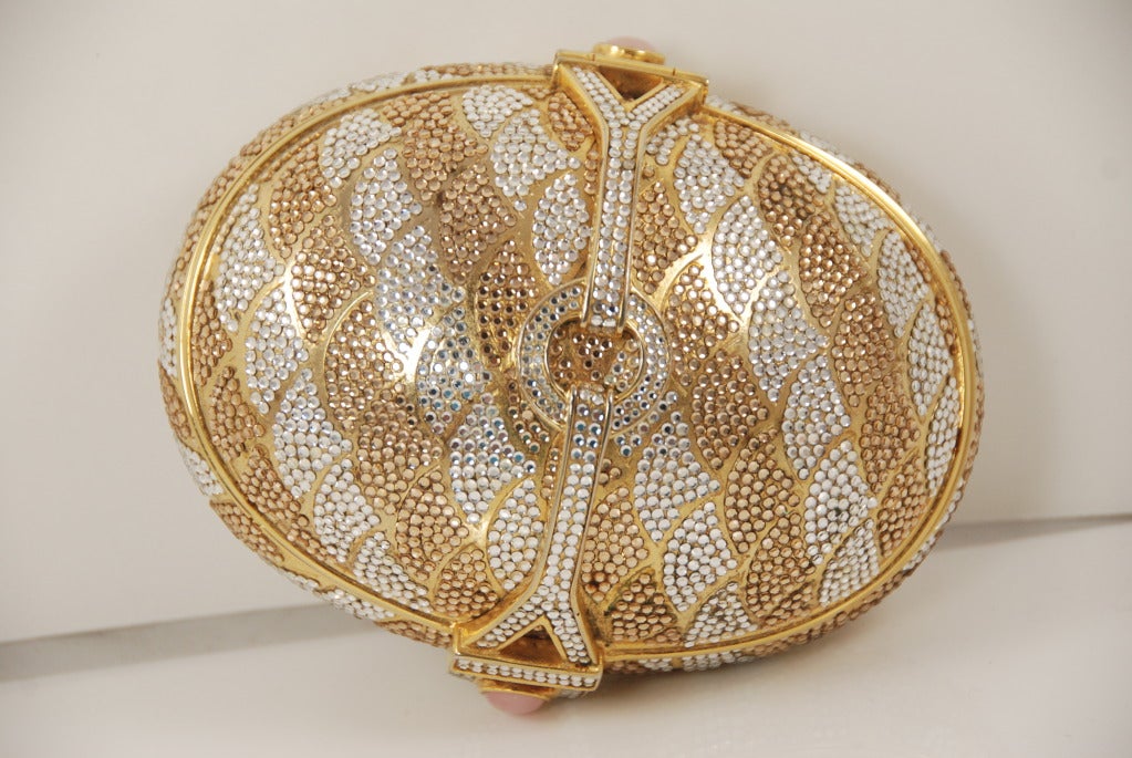 Judith Leiber oval gold and clear rhinestone minaudiere from the 1980s.  The clasp is quartz. The design is symmetrical but only one side opens. The clasp works by slightly pressing in on the bottom half of the purse while lifting the top (easier